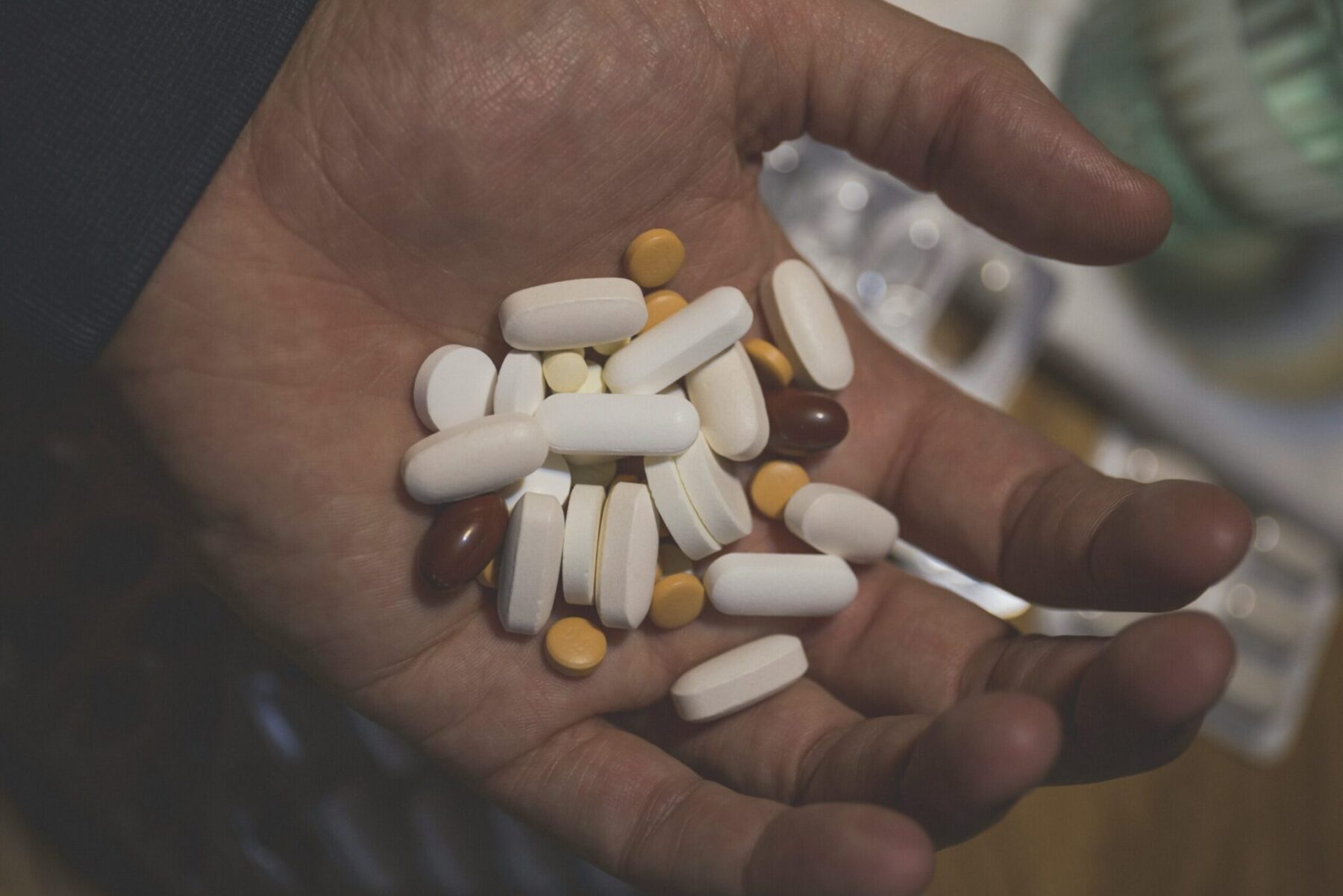 Hand mit verschiedenen Tabletten und Kapseln